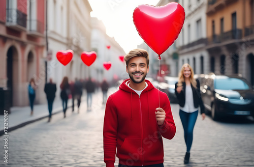 A young Asian man holds balloons in the form of red hearts in his hand, a young brunette blonde woman stands in front of him and smiles, © Yury Fedyaev