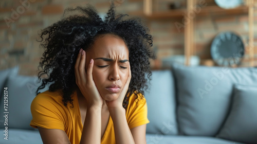 Unhappy  young woman touching her head and suffering from headache. Young woman suffering from strong headache or migraine sitting at home photo