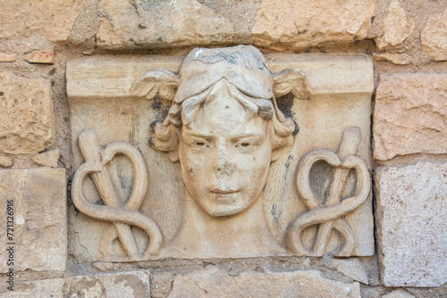 Stone-carved head of Hermes with wings rising from his hair and caduceus on both sides on the ruins of an ancient Roman time wall in Spain