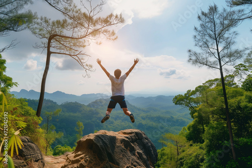 Life style concept with a happy young man withhis arms up, jumps on the top of a mountain to celebrate a successful hike.