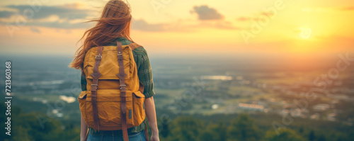 young woman hiker with backpack standing on top of mountain and looking at beautiful sunset