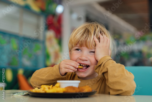 Canvas Print happy boy with blond hair eats fries and nuggets in restaurant