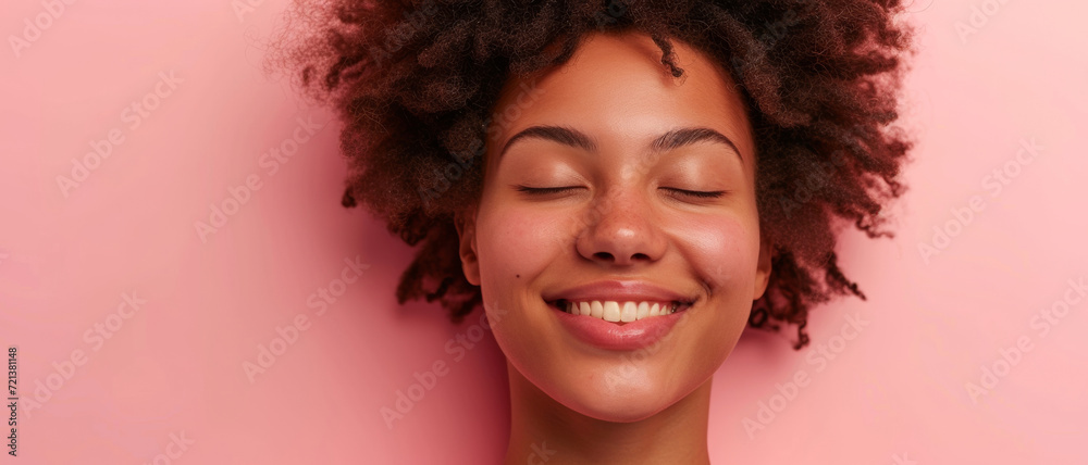 A joyful expression blossoms on her face, as her eyes close in contentment against a blush pink backdrop A joyful expression blossoms on her face, as her eyes close in contentment against a blush pink backdrop