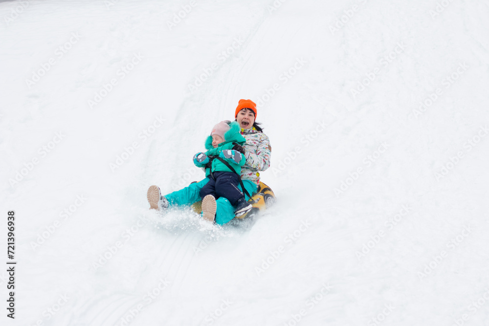 mom and daughter are riding a snow slide in the forest. Snow-white winter