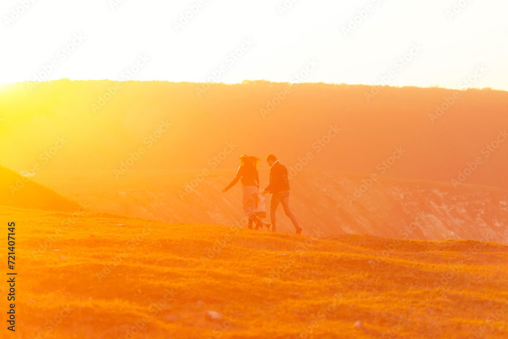 Young loving parents are walking on a field with their little daughter at sunset.
