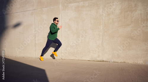 Adult athletic man running fast along concrete wall in the city