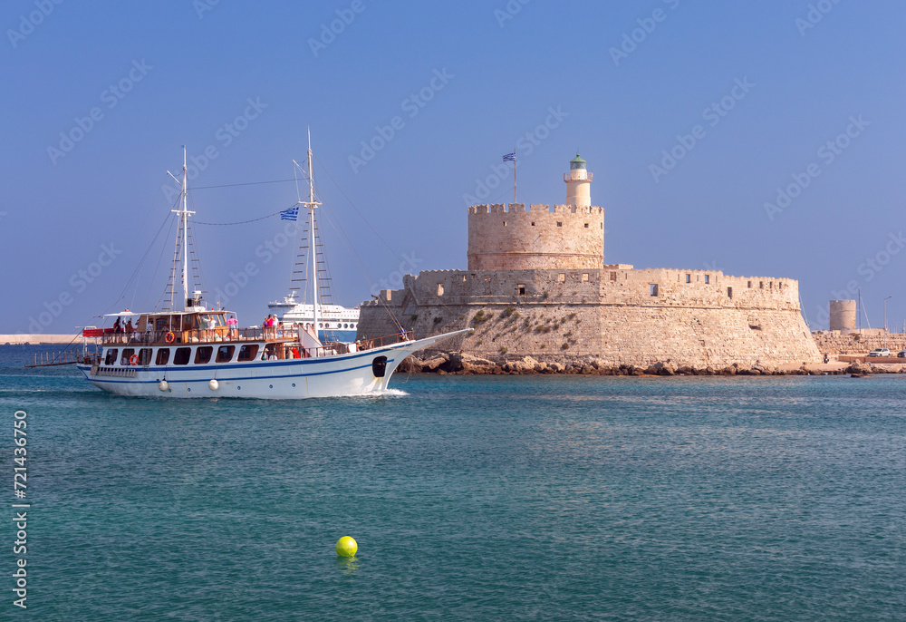 Pleasure tourist boat against the backdrop of the old lighthouse at Fort St. Nicholas in Rhodes.