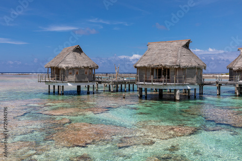French Polynesia atoll with typical overwater bungalows and pink coral reef in full sun light.