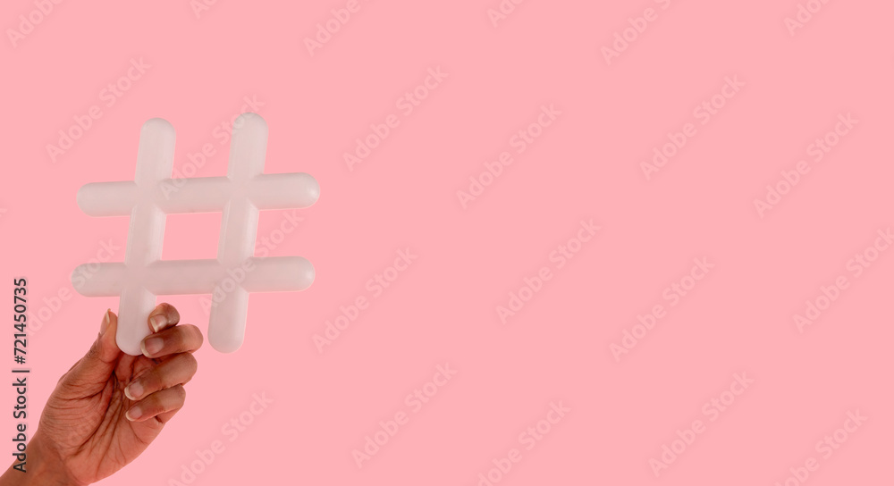 Obraz premium woman holding sign hashtag in her hand on pink background with copy space. social media, blogging and viral topics on internet concept