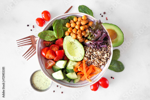 Healthy homemade salad bowl with avocado, chickpeas, quinoa and vegetables. Overhead view with frame of ingredients on a white marble background.