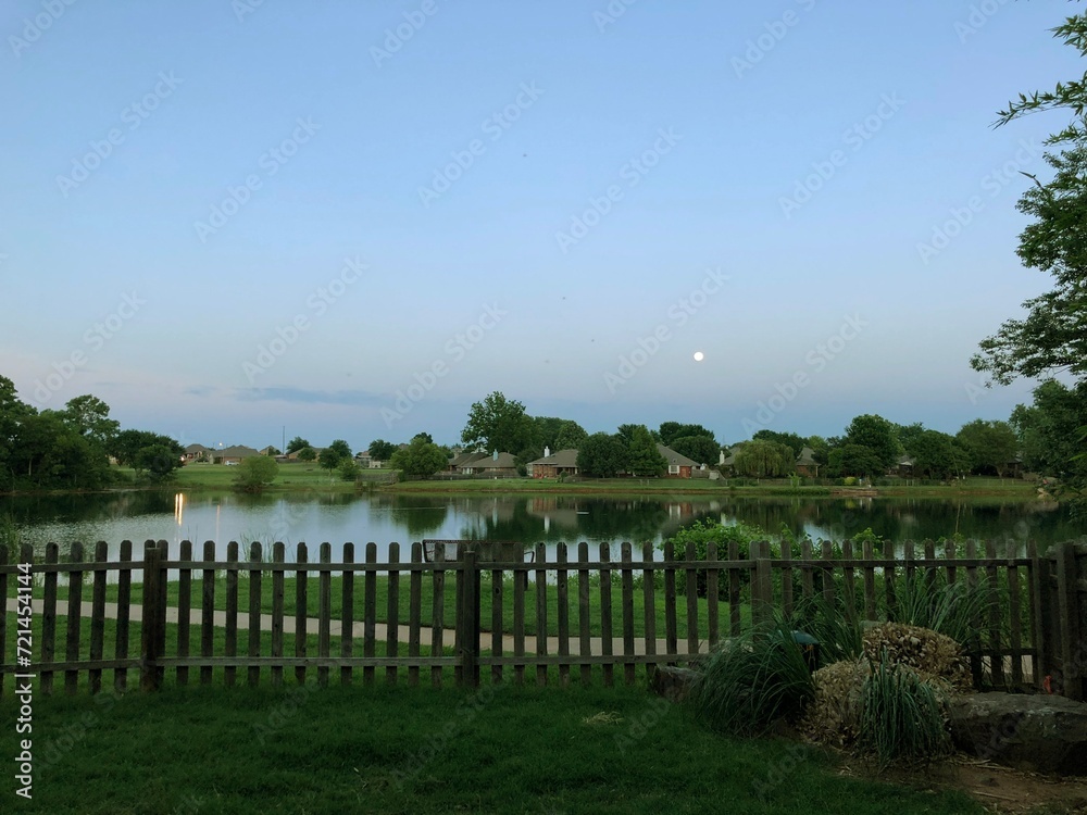 A view of a lake with a fence and a house in the background A view of a lake with a fence and a house in the background