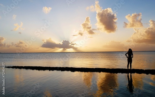 Beautiful sunset reflected in the waters, with the silhoutte of an unrecognizable woman standing on the rocks.