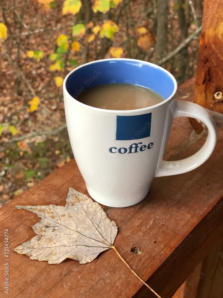 Coffee cup and dry leaf on wooden table in autumn forest