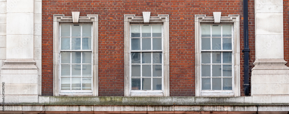 three aligned classic white windows of typical London architecture with red brick wall