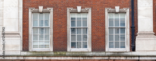 three aligned classic white windows of typical London architecture with red brick wall