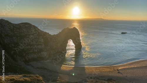 The sun goes down on the Jurassic coast and Durdle Door in Dorset with Seak Pink Trift growing on the top of the cliff in the foreground. Durdle Door, Dorset, Jurassic Coast, England, UK photo