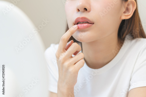 Lip care concept, worried asian young woman finger touching lips in front of mirror after applying lipstick balm on dry mouth from natural beauty product, skincare routine, makeup and cosmetics. photo