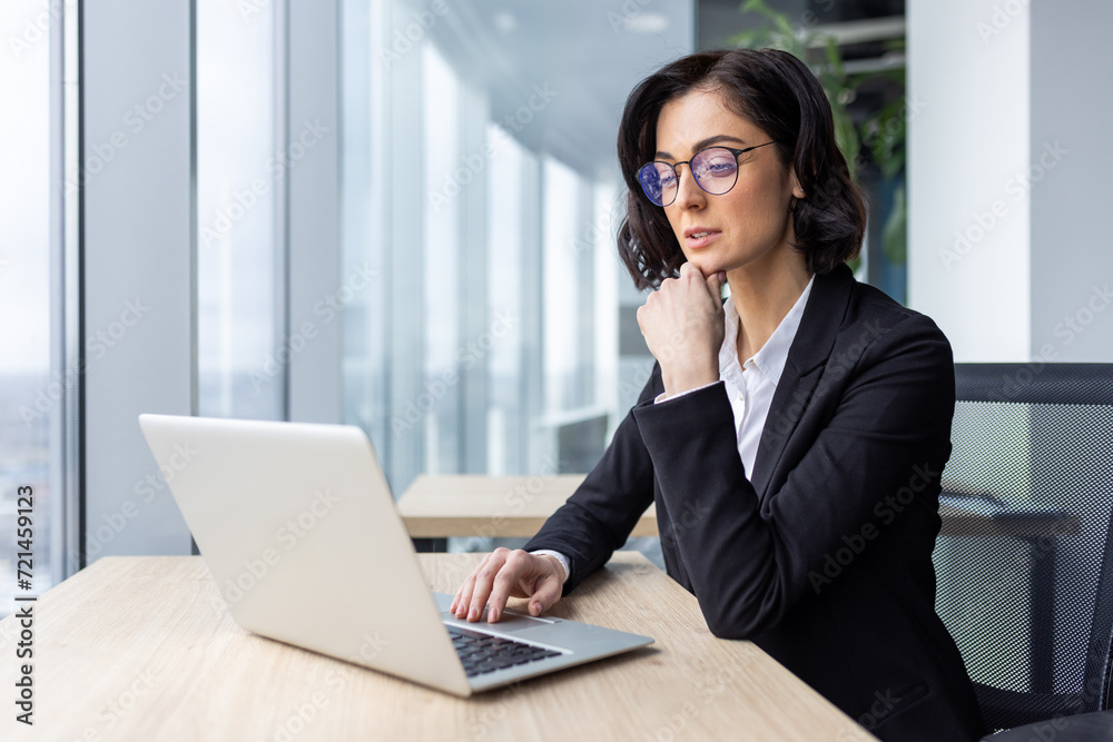Serious businesswoman boss thinking working with laptop inside office near window, female office worker in business suit typing ideas on keyboard, looking at screen reading and solving current tasks Serious businesswoman boss thinking working with laptop inside office near window, female office worker in business suit typing ideas on keyboard, looking at screen reading and solving current tasks