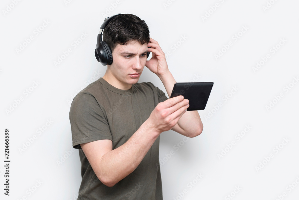 College student, young guy studying online, looking at tablet and fixing wireless headphones, guy looking at tablet in concentration, online education College student, young guy studying online, looking at tablet and fixing wireless headphones, guy looking at tablet in concentration, online education