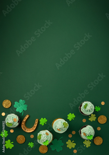 St. Patrick's Day vanilla and chocolate cupcakes with green frosting and  shiny clover decorations on green paper background. Irish holiday dessert concept. Top view, copy space.