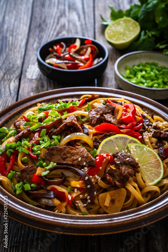 Asian style stir fried vegetables, roast beef and chow mein noodles on wooden table 