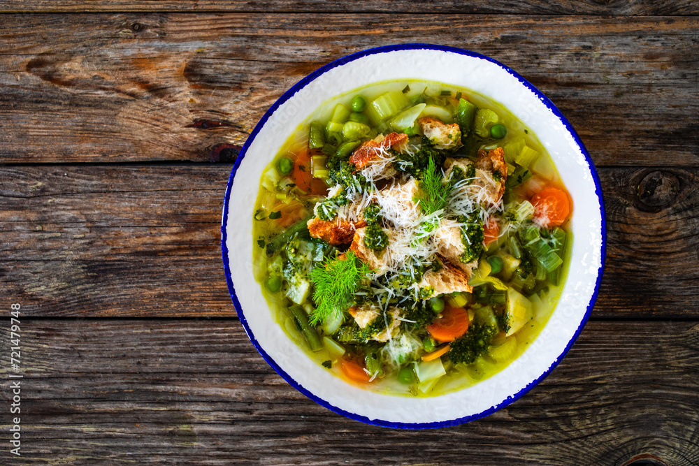 Pistou soup Nice - broth with basil pesto, bread, cheese and vegetables on wooden background in white bowl

