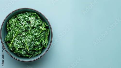 A bowl of vibrant green spinach leaves on a soft teal background, emphasizing freshness and health
