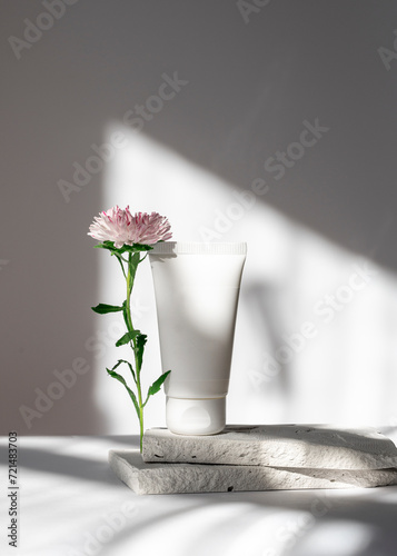 A white tube of cream or body lotion, on a piece of stone on a light background with a flower. Natural cosmetic. Therapeutic spa skin care. Healthcare and medicine concept.