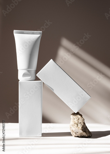 White tube of body cream or lotion along with packaging on a stone on a beige background. Natural cosmetic.