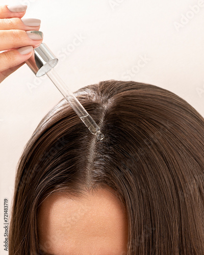 A young woman applies a drop of oil from a pipette to her scalp, close-up. Vitamins, keratin for treatment, strengthening and growth of hair. Problems with dandruff, hair loss. Hair care concept 