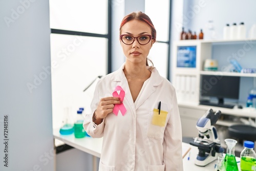 Young caucasian woman scientist holding pink cancer ribbon at laboratory