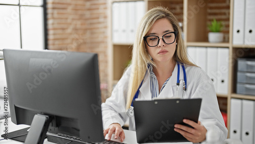 Young blonde woman doctor using computer reading medical report at clinic photo