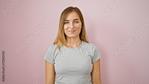 Joyful young blonde woman exuding confidence, laughing and standing over a pink isolated background in a fun portrait