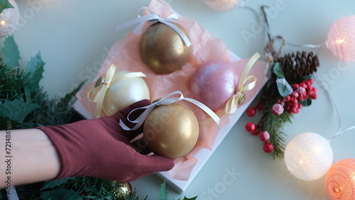 Female hand in glove stacking chocolate balls of different colors in a gift box. Chocolate balls in a box