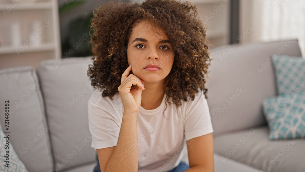 Young beautiful hispanic woman sitting on sofa with serious expression at home Young beautiful hispanic woman sitting on sofa with serious expression at home