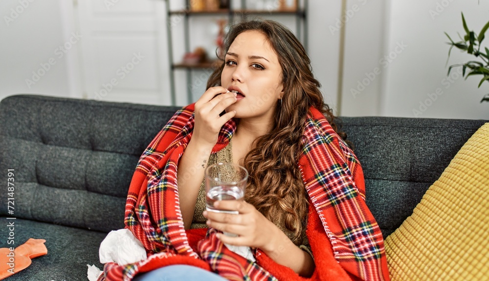 Naklejka premium Young beautiful hispanic woman taking pills sitting on sofa at home