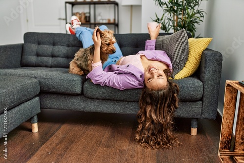 Young beautiful hispanic woman lying on sofa with dog holding cup of coffee at home photo
