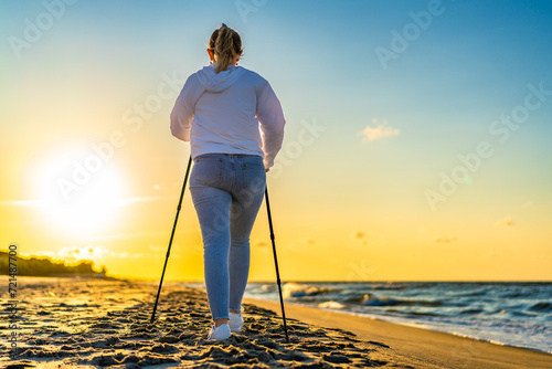 Nordic walking - beautiful woman exercising on beach at sunset