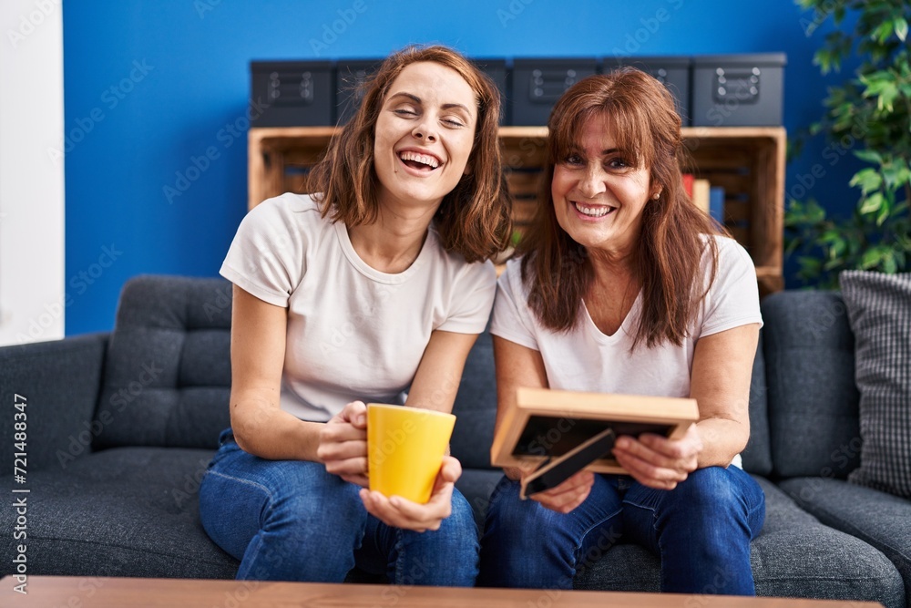 Two women mother and daughter drinking coffee looking photo at home