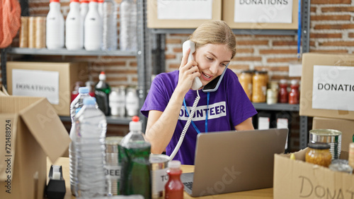 Young blonde woman volunteer talking on smartphone and telephone using laptop at charity center