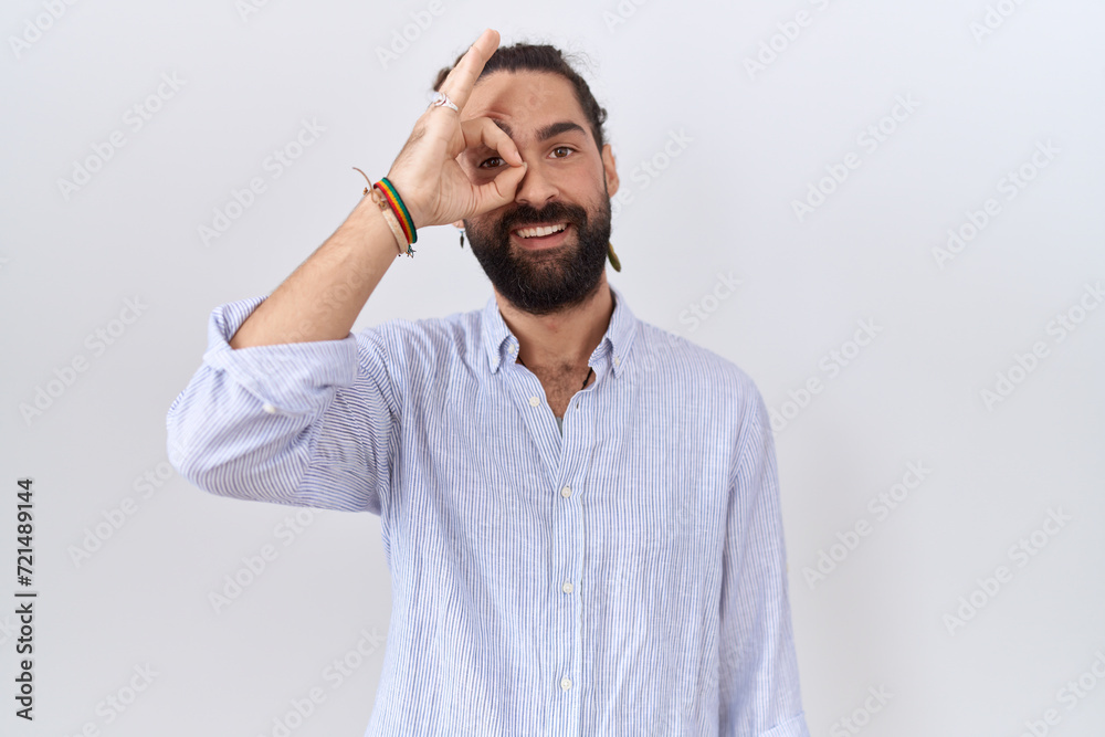 Fototapeta premium Hispanic man with beard wearing casual shirt doing ok gesture with hand smiling, eye looking through fingers with happy face.