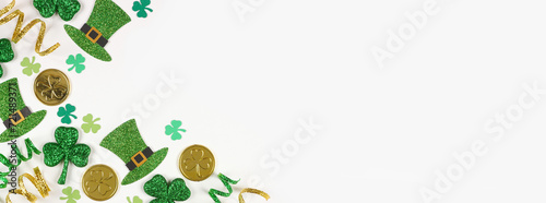 St Patricks Day corner border of green shamrocks, leprechaun hats, gold coins and ribbon. Overhead view over a white banner background with copy space.