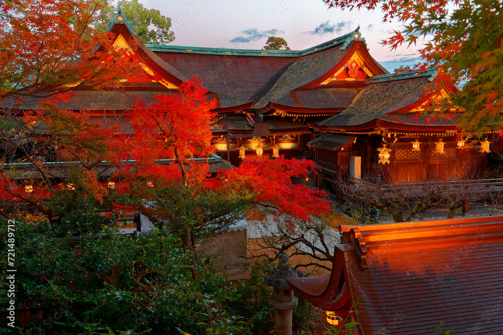 Obraz premium Beautiful autumn scenery of maple trees by majestic traditional Japanese architectures in Kitano Tenmangu, a famous Shinto Shrine (Jinja) in Kyoto, Japan, with fiery foliage lighted up before dusk