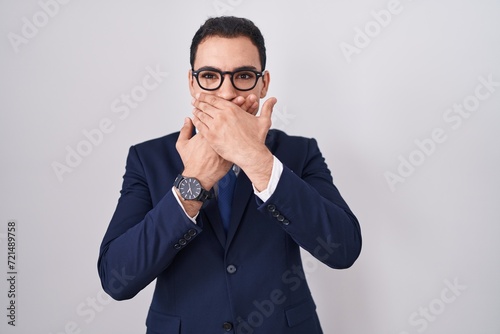 Young hispanic man wearing suit and tie shocked covering mouth with hands for mistake. secret concept.