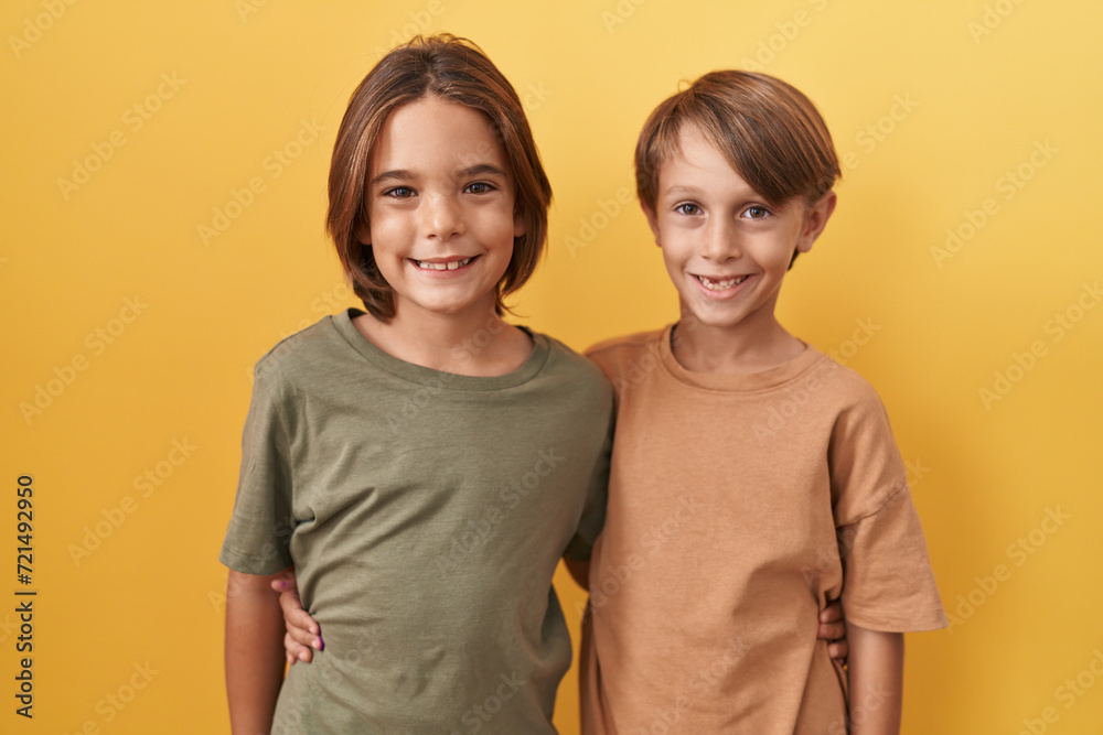 Two adorable boys, standing and hugging together on an isolated yellow background, radiating joy with their confident, toothy smiles and positive attitude. Two adorable boys, standing and hugging together on an isolated yellow background, radiating joy with their confident, toothy smiles and positive attitude.