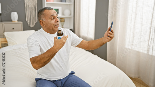 Mature hispanic man checking blood sugar level with glucometer while sitting on bed in a bedroom. photo