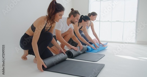 group of Young beautiful fit sport people folding mats for yoga class session at sport studio