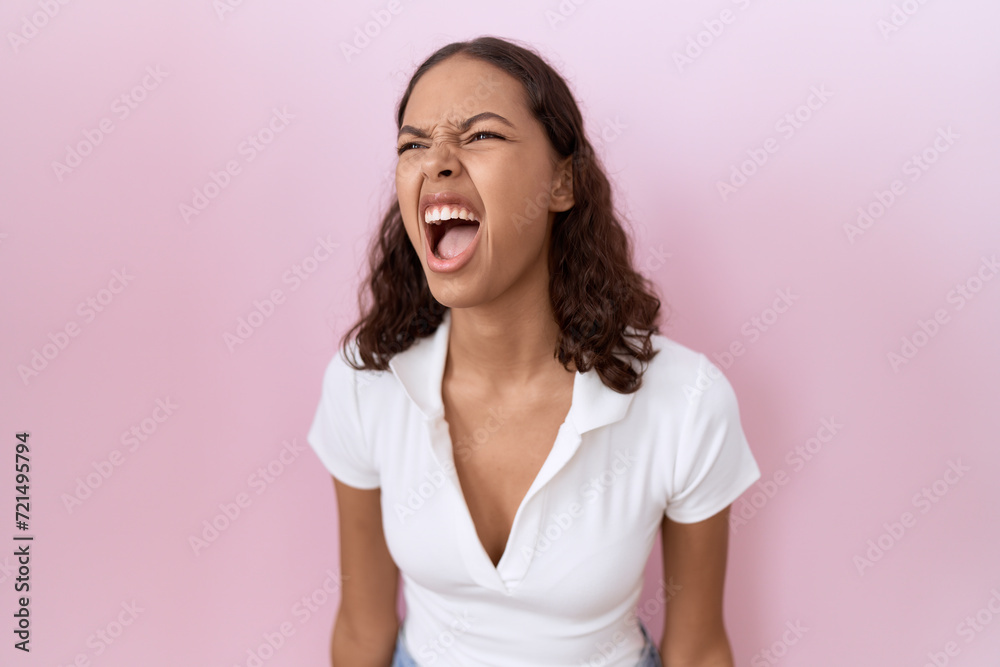 Young hispanic woman wearing casual white t shirt angry and mad screaming frustrated and furious, shouting with anger. rage and aggressive concept. Young hispanic woman wearing casual white t shirt angry and mad screaming frustrated and furious, shouting with anger. rage and aggressive concept.