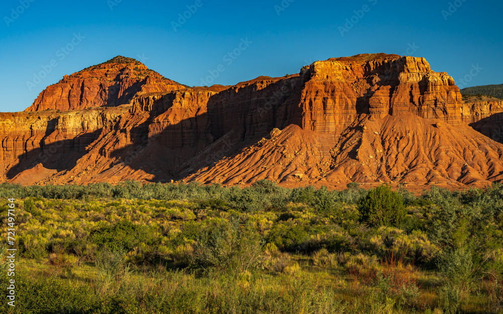 Red rock cliffs of Capitol Reef national park illuminated by a strong sunlight in Utah early in the morning. Red rock cliffs of Capitol Reef national park illuminated by a strong sunlight in Utah early in the morning.