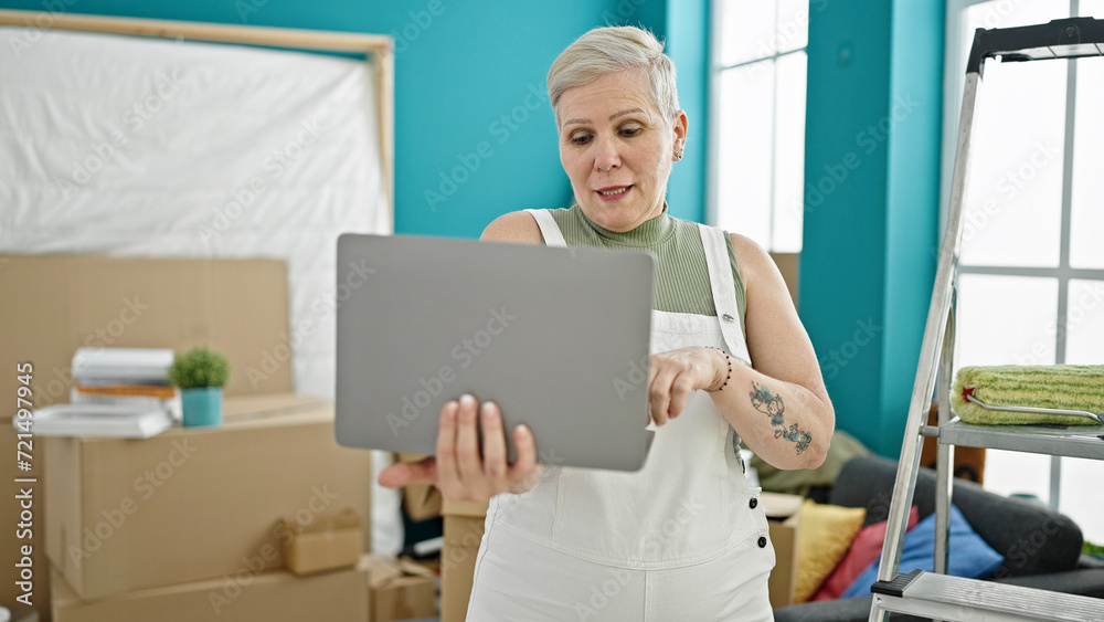 Middle age grey-haired woman using laptop standing at new home Middle age grey-haired woman using laptop standing at new home
